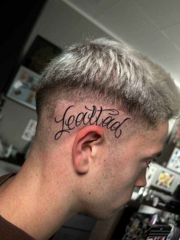 Script on head tattoo by Alex, artist at Fattys Tattoos & Piercings